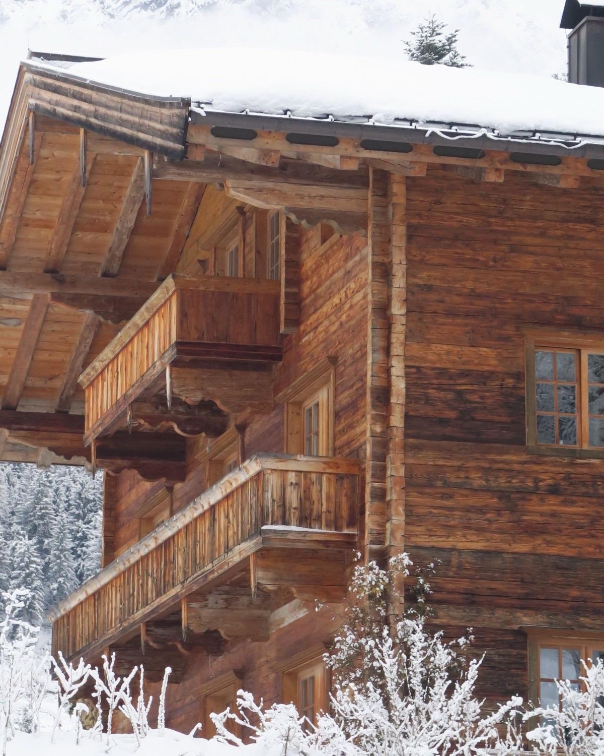 La façade d’un vieux chalet de bois sous la neige, ses balcons étagés et ses fenêtres éteintes.