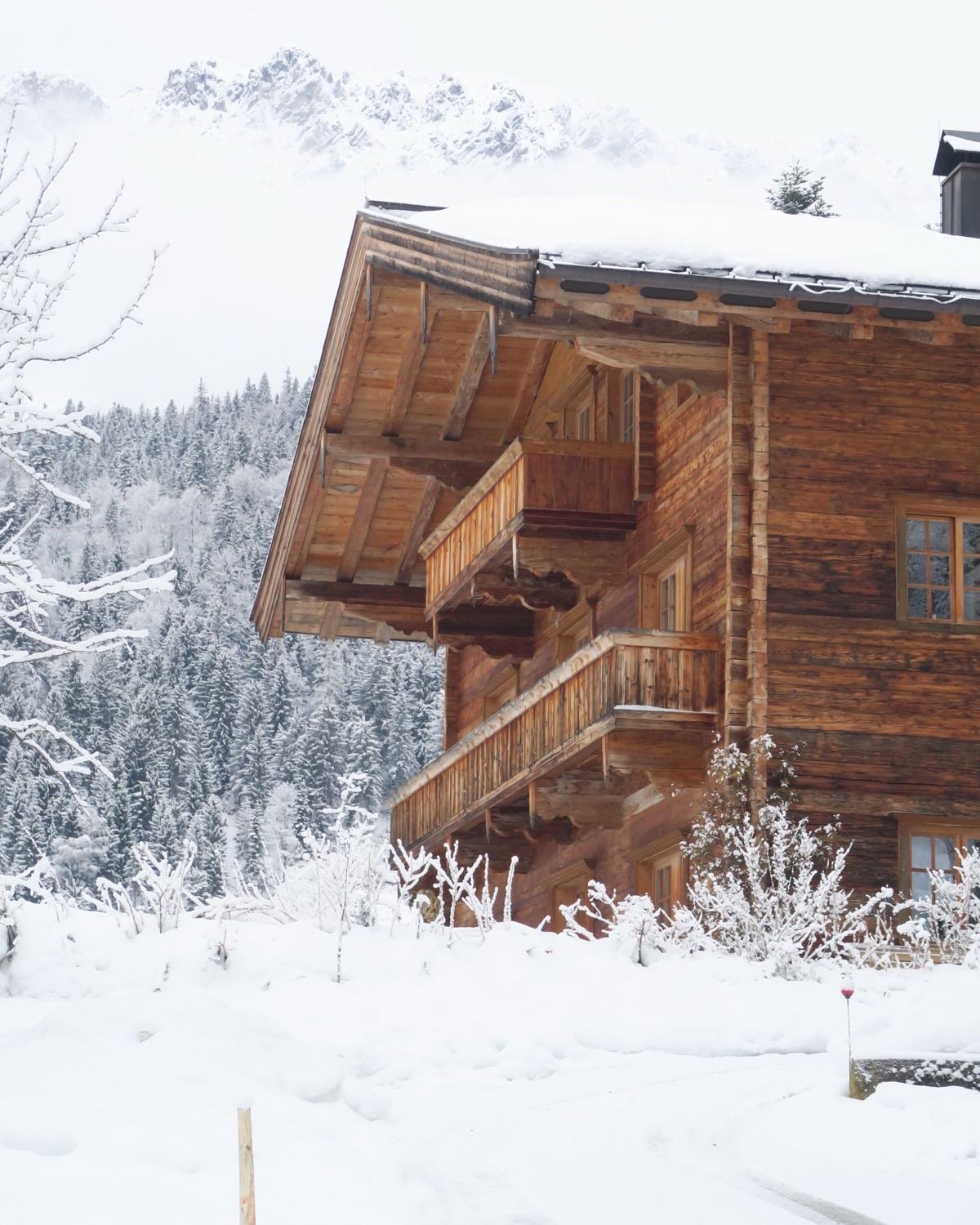 Un vieux chalet de bois sous la neige fraîche, du faîte à la base, la forêt givrée et les sommets dans la brume.